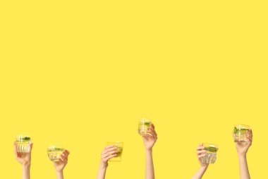 Sarı arka planda farklı bardaklarda taze mojito içen kadın elleri.