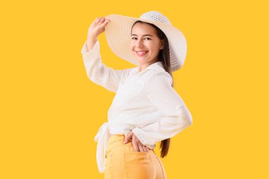 Sarı arka planda yaz şapkalı şık genç kadın.