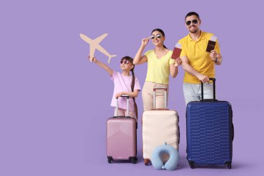 Kağıt uçak ve leylak arka planda valizleri olan turist ailesi.