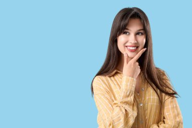 Mavi arka planda güzel gülüşü olan düşünceli genç bir kadın.