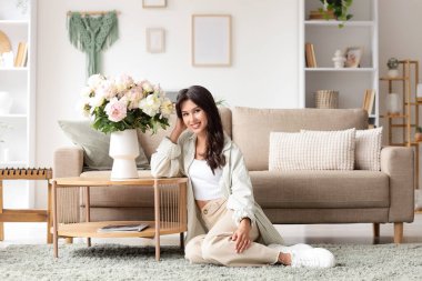 Evdeki masada elinde şakayık çiçekleri olan genç bir kadın.