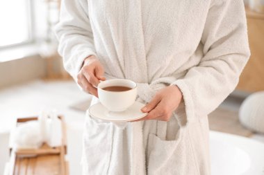 Yumuşak bornozlu genç bayan evde bir fincan çayla, yakın plan.