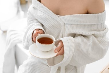 Waffle bornozlu genç bayan evde bir fincan çayla, yakın plan