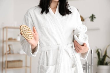 Evde havluları ve masaj fırçası olan yumuşak bornozlu genç bir kadın.