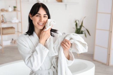 Evde bornozlu genç bir kadın var.