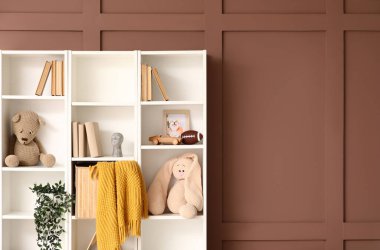 Oyuncak ve kitaplarla dolu raflar kahverengi duvarın yanında.