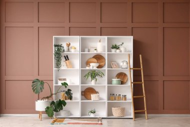 Mutfak gereçleri, bitkiler ve merdiveni olan raf ünitesi odada kahverengi duvarın yanında.