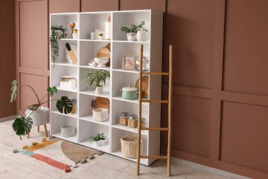 Mutfak gereçleri, bitkiler ve merdiveni olan raf ünitesi odada kahverengi duvarın yanında.