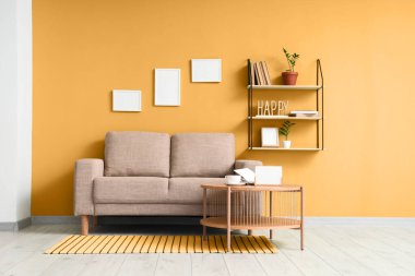 Oturma odasının iç tarafındaki yeşil duvarın yanındaki tahta sehpa ve gri kanepe.