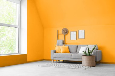 Oturma odasının içinde kanepe, hasır masa, raf ve çiçek var.