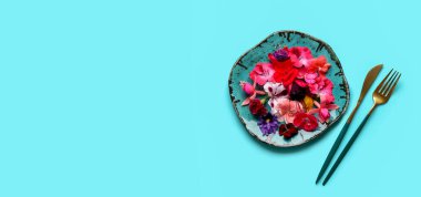 Farklı güzel, yenilebilir çiçekli tabaklar ve mavi arka planda çatal bıçaklar.