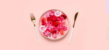 Güzel çiçekli tabak ve pembe arka planda çatal bıçak takımı.