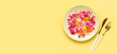 Farklı güzel, yenilebilir çiçekli tabaklar ve sarı arka planda çatal bıçak takımı.