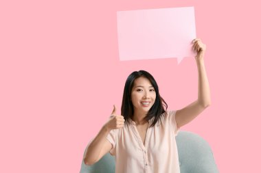 Güzel Asyalı kadın, boş konuşma baloncuğuyla pembe arka planda baş parmağını kaldırıyor.