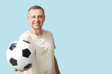 Mavi arka planda futbol topu olan yakışıklı olgun bir adam.