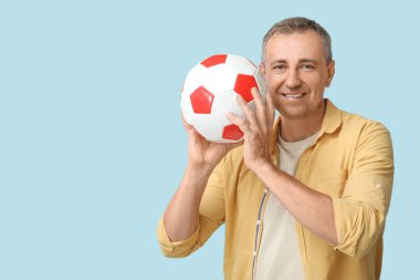 Yakışıklı olgun bir adam mavi arka planda futbol topuyla oynuyor.