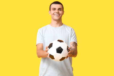 Sarı arka planda futbol topu olan yakışıklı genç adam.