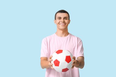 Mavi arka planda futbol topu olan yakışıklı genç adam.