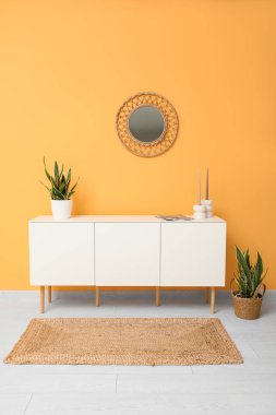 Çağdaş beyaz çekmeceler içinde ev bitkileri ve turuncu duvarın yanındaki aynalar.