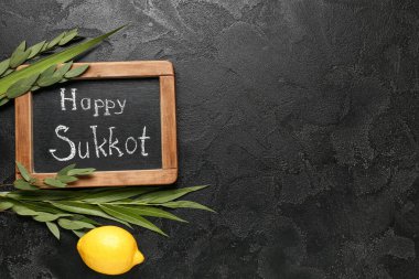 Dört tür (lulav, hadas, arava, etrog) ve siyah grunge arkaplan üzerinde HAPPY SUKKOT yazılı kara tahta