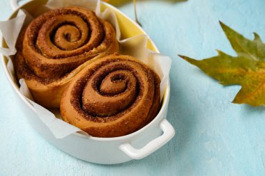 Lezzetli tarçınlı çörekler ve mavi arka planda sonbahar yaprağı.