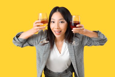 Sarı arka planda şarap kadehleri olan güzel Asyalı iş kadını.