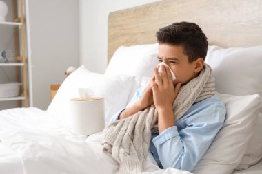 Yatak odasında hapşıran peçeteli hasta çocuk.