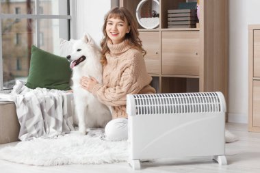 Samoyed köpekli genç bir kadın radyatörün yanında ısınıyor.