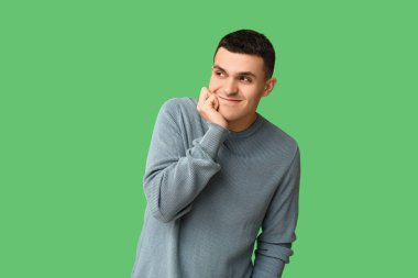 Yeşil arka plandaki yakışıklı, utangaç genç adam.