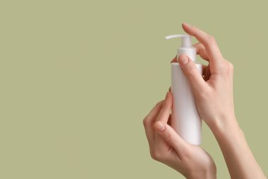 Yeşil arka planda krem şişesi olan kadın eller, yakın plan.