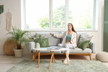 Oturma odasındaki gri kanepede oturan genç kadın.