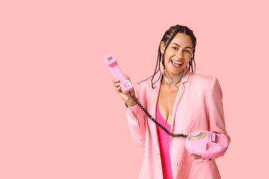 Pembe arka planda elinde eski bir telefon tutan zarif Afro-Amerikalı kadın.