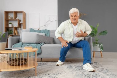 Olgun bir adam evdeki koltukta kalp krizi geçiriyor.