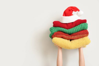 Beyaz duvarın yanında Noel Baba şapkası olan kışlık elbiseleri tutan kadın.