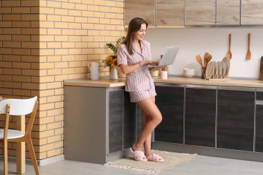 Genç bir kadın mutfakta dizüstü bilgisayar kullanıyor.