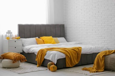 Yatak odasının içinde sonbahar dekoru olan büyük yatak ve komodinli bir masa.