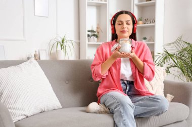 Kulaklıklı, Chia tohumu pudingli genç bir kadın evdeki kanepede oturuyor.