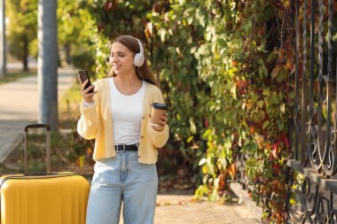 Kulaklıklı ve kahveli bir bayan turist sonbahar günü parkta cep telefonu kullanıyor.