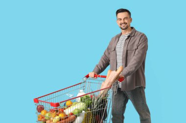 Mavi arka planda alışveriş arabası olan mutlu genç bir adam.
