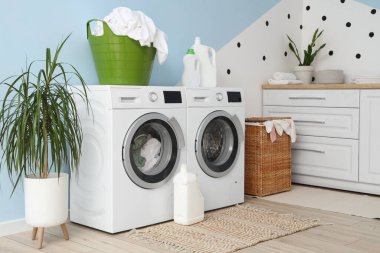 Çamaşır makineleri, deterjanlar ve sepetlerle çamaşır odasının içinde.