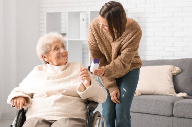 Genç hemşire evde tekerlekli sandalyedeki yaşlı kadına hap veriyor.