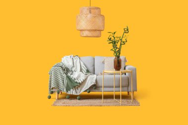 Vazoda bambu saplı masa, kanepe ve sarı arka planda lamba.