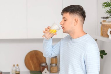 Genç adam mutfakta limonlu su içiyor.