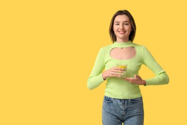 Sarı arka planda bir bardak limonlu su ile güzel genç bir kadın.