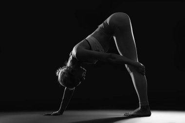 Siyah arka planda yoga yapan genç bir kadının silueti.