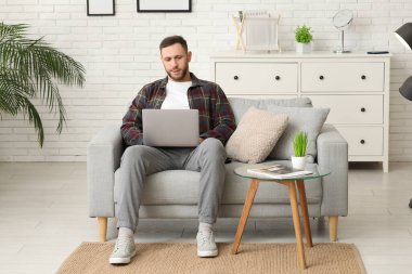 Oturma odasında kanepede otururken laptop kullanan yakışıklı adam.