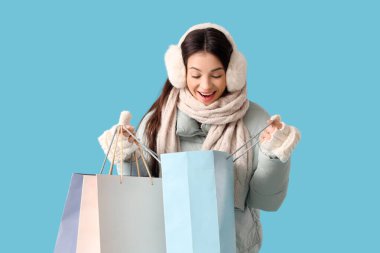 Mavi arka planda alışveriş torbaları olan, kalın elbiseli genç bir kadın.