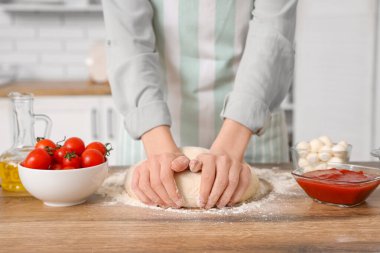 Mutfakta masanın yanında pizza için hamur yoğuran bir kadın.