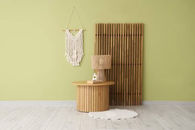 Halı, lamba ve dekorlu şık kahve masası açık yeşil duvarın yanında.