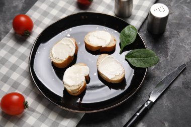 İşlenmiş peynirli lezzetli bruschetta tabağı, ıspanak yaprakları ve siyah arka planda taze domatesler.